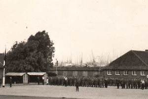 Manschappen bij de vlaggenmast op de appélplaats van Kamp Zeeburg, circa 1955.
